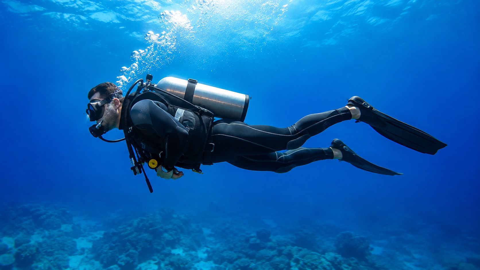 A professional scuba diver swimming gracefully over a vibrant coral reef in clear deep blue water.